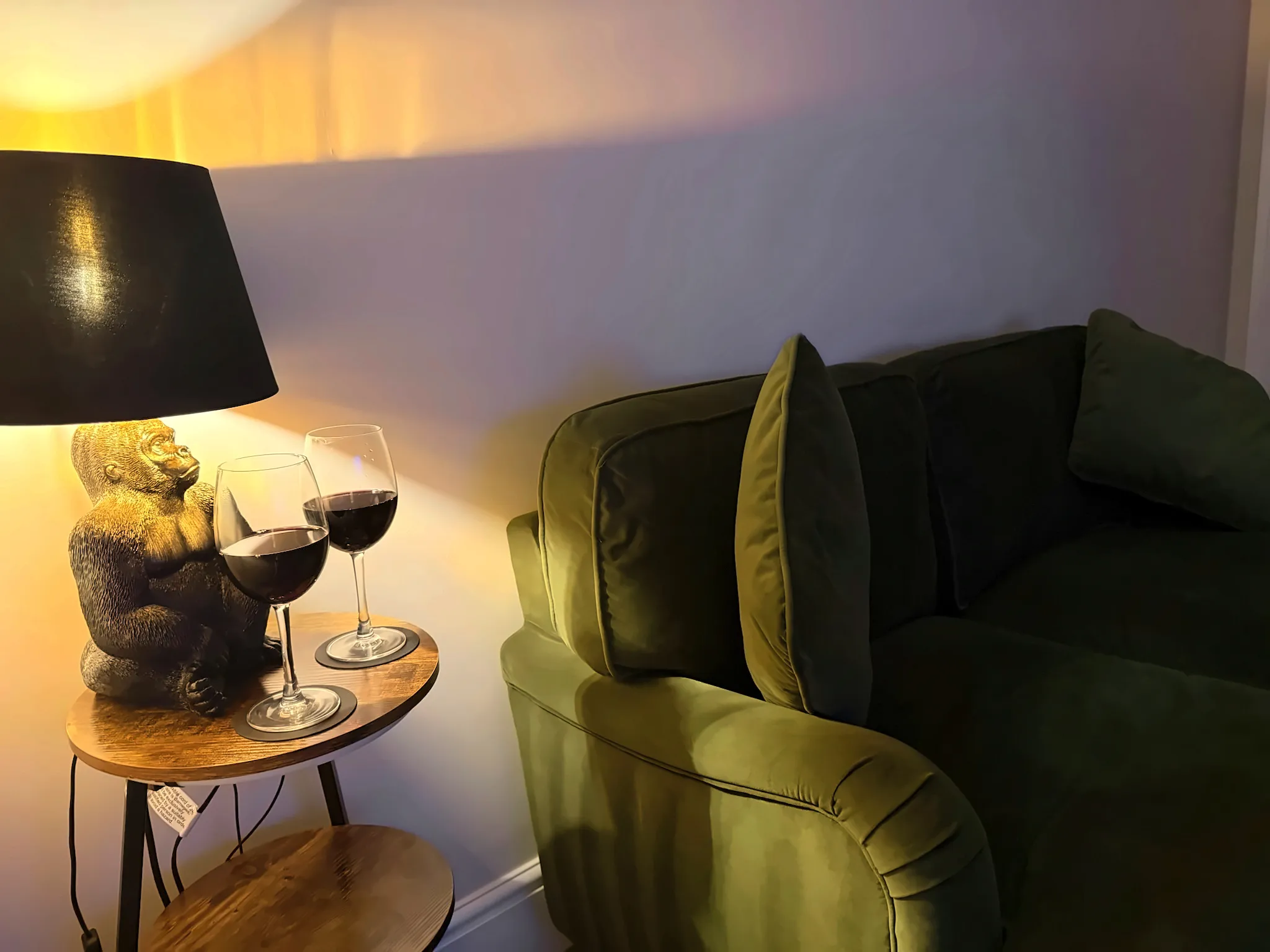 A lamp-lit corner of the sitting room, with two glasses of red wine beside the green sofa